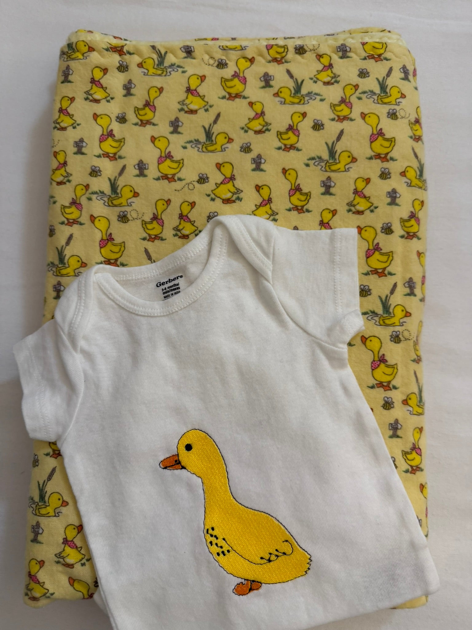 White baby onesie with a yellow duck design on a yellow fabric with duck pattern